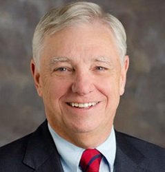 Headshot of Rick Gilfillan. Rick wears a suit and red tie.