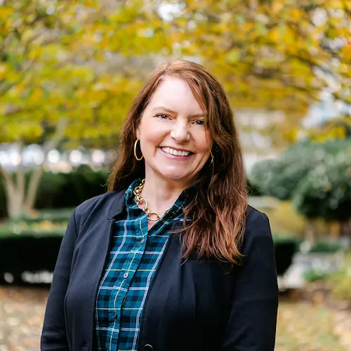 Headshot of Anna Christ. Anna wears a plaid shirt and a black blazer.