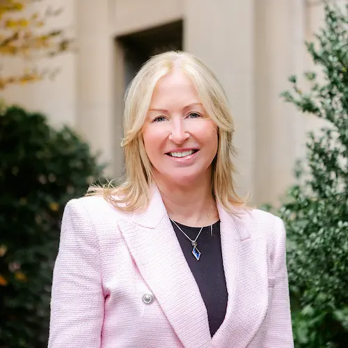 Headshot of May-Lynn Andresen. May-Lynn wears a black shirt and a pink blazer.